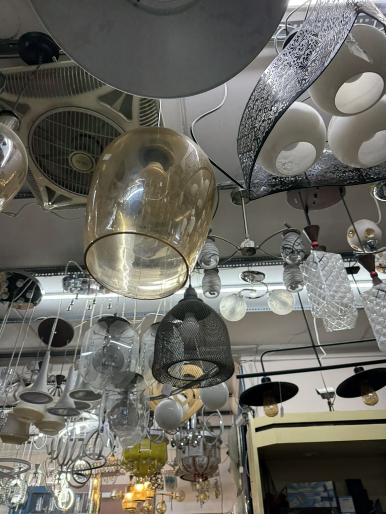 Rows of glass and brass pendants hanging close together under the shop's strip lights, with no labels or prices.